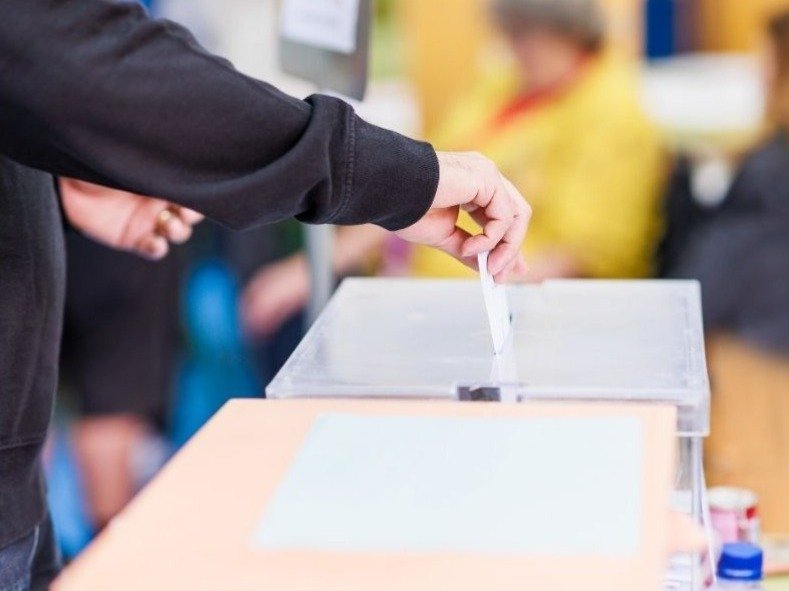 Mensch steckt Wahlzettel in Wahlurne