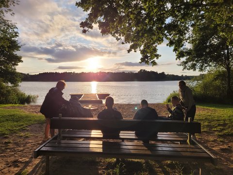 Sonnenuntergang am See. Gruppe von Menschen, ein Mensch im Rollstuhl. 