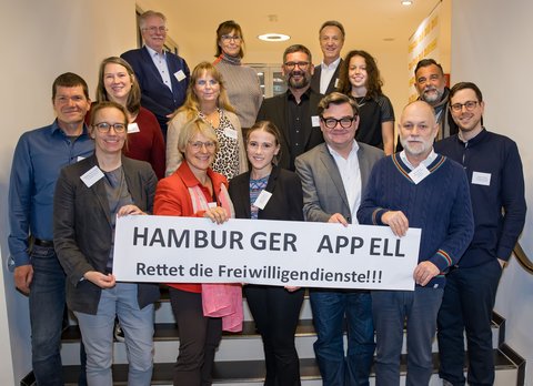Ca. 15 Menschen halten ein Schild "Hamburger Appell - Rettet die Freiwilligendienste"