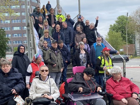 Menschen vor und auf einer Brücke. Darunter Rollstuhlfahrer*innen.