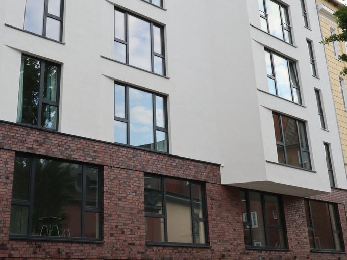 Mehrstöckiges Wohngebäude mit weißen Fassaden und großen Fenstern, Erdgeschoss aus rotem Backstein