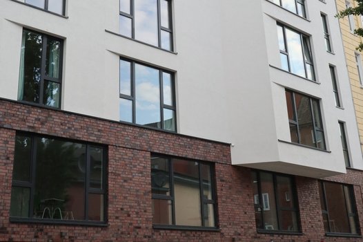 Mehrstöckiges Wohngebäude mit weißen Fassaden und großen Fenstern, Erdgeschoss aus rotem Backstein