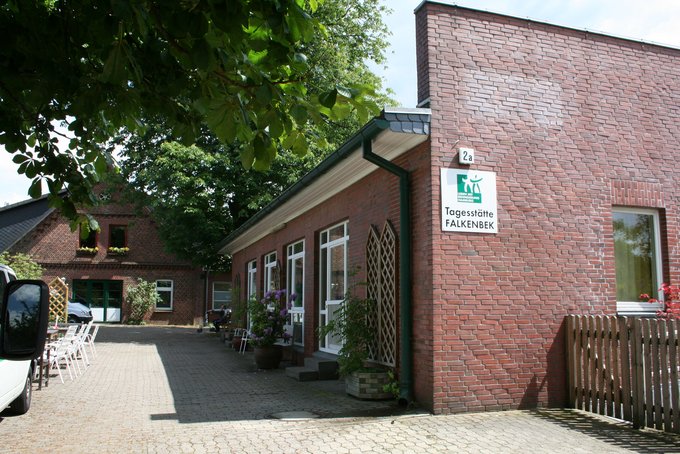 Backsteingebäude mit Schrägdach und mehreren Fenstern neben gepflastertem Weg unter Bäumen