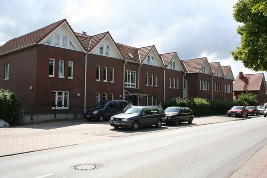 Reihe von roten Backsteinhäusern mit weißen Dachgiebeln an einer Straße mit parkenden Autos