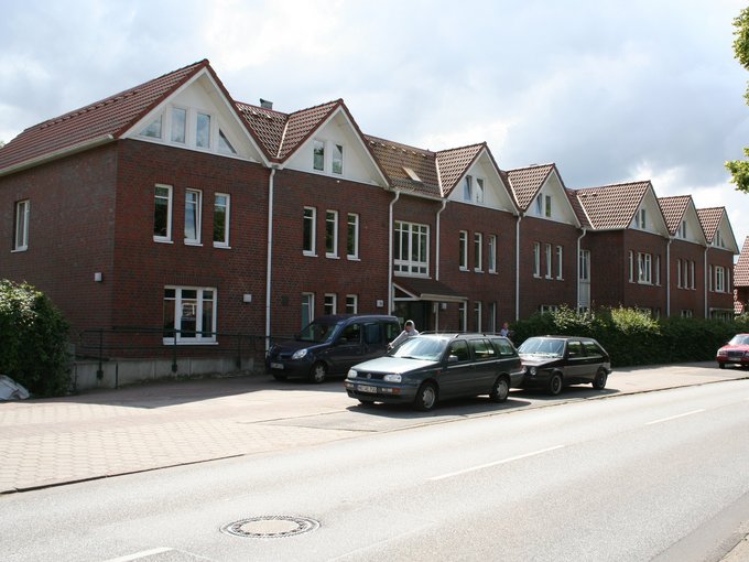 Reihe von roten Backsteinhäusern mit weißen Dachgiebeln an einer Straße mit parkenden Autos