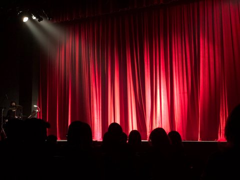 Theaterbühne mit geschlossenem Vorhang und Publikum im Vordergrund