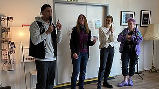 Drei Wochen und ein Mann mit Mikro tragen etwas vor.
