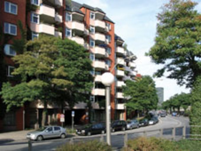 Mehrstöckiges Wohngebäude mit Balkonen an einer Straße mit parkenden Autos und Bäumen