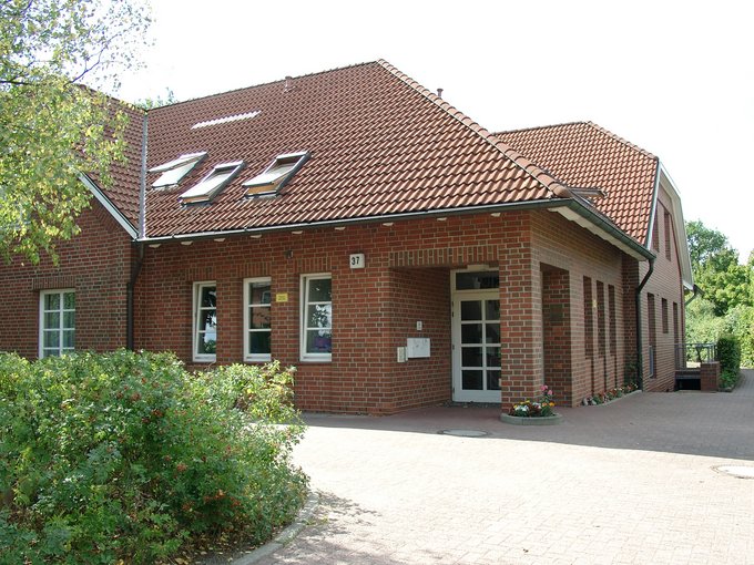 Backsteinhaus mit geschwungenem Ziegeldach und mehreren Fenstern, umgeben von Büschen