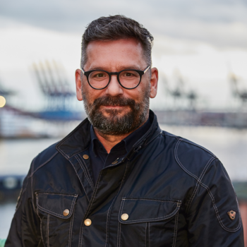 Ein Foto von Ralph Grevel. Im Hintergrund sieht man den Hamburger Hafen.