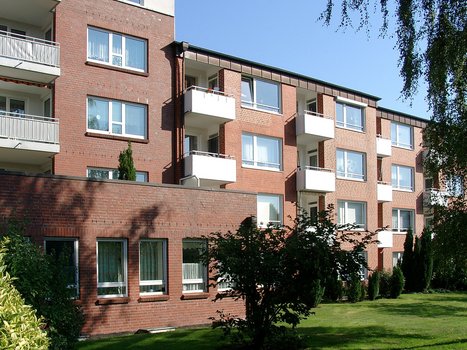 Mehrstöckiges Wohngebäude aus rotem Backstein mit Balkonen und grüner Wiese im Vordergrund