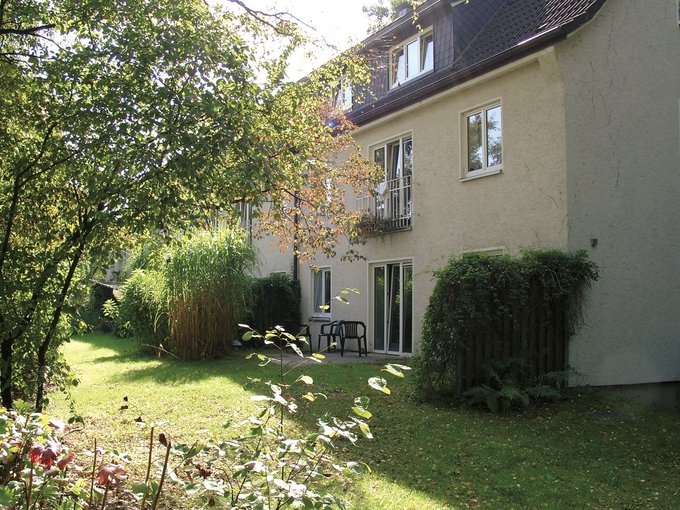 Haus mit gelber Fassade und Garten mit Bäumen und Rasen im Vordergrund