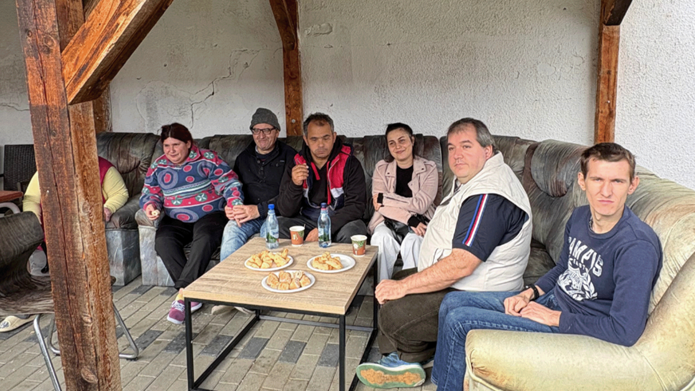 Gruppenbild von sieben Menschen auf einer Sofalandschaft in ihrer Wohneinrichtung in Cadea/Rumänien