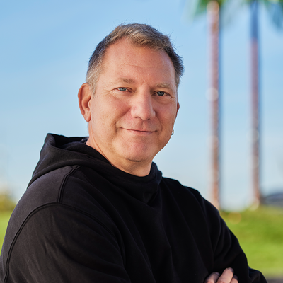 Ein Mann steht mit verschränkten Armen vor künstlichen Palmen und lacht