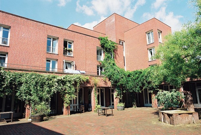 Backsteingebäude mit mehreren Fenstern und begrüntem Innenhof unter blauem Himmel