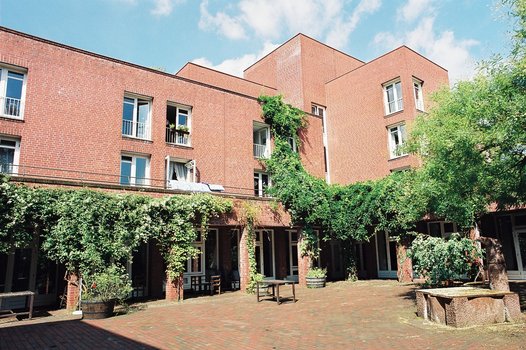 Backsteingebäude mit mehreren Fenstern und begrüntem Innenhof unter blauem Himmel