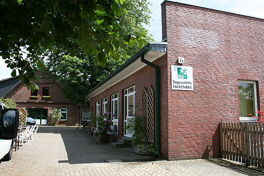 Backsteingebäude mit Schrägdach und mehreren Fenstern neben gepflastertem Weg unter Bäumen