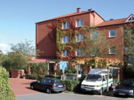 Mehrstöckiges rotes Backsteingebäude mit Efeu an der Fassade, davor geparkte Autos