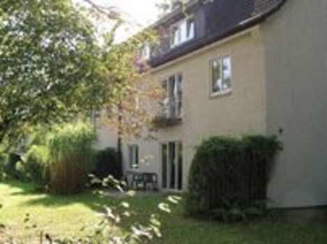 Haus mit gelber Fassade und Garten mit Bäumen und Rasen im Vordergrund