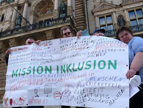 Menschen protestieren mit Plakat für Inklusion.