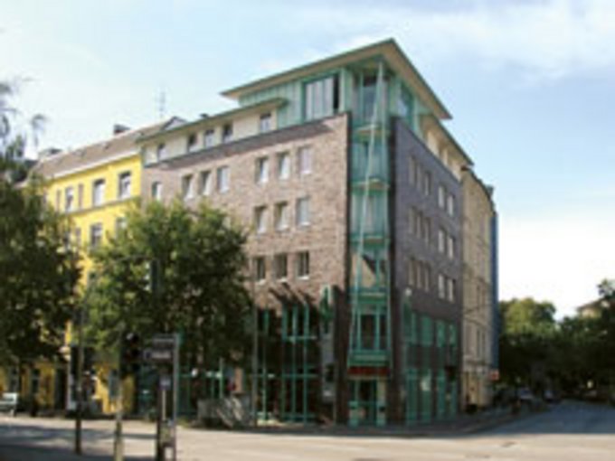 Modernes Wohnhaus an Straßenecke mit großen Fenstern und heller Fassade.