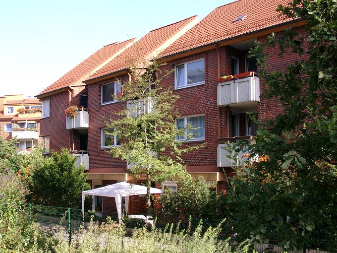 Mehrstöckiges Wohngebäude mit roten Ziegeln, weißen Balkonen und grünem Garten im Vordergrund