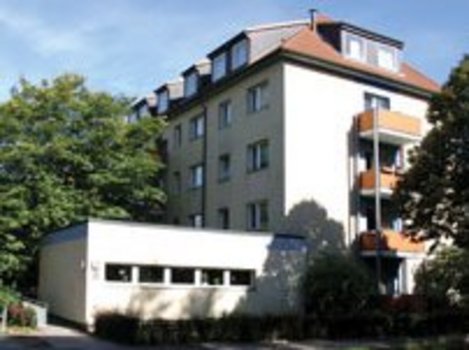 Mehrstöckiges Wohngebäude mit Balkonen, umgeben von Bäumen