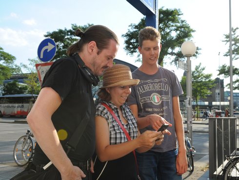 Zwei Männer und eine Frau schauen auf ein Handy.