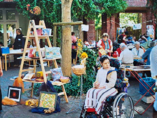 Menschen mit Behinderung und Mitarbeiter*innen zeigen im Innenhof vom Südring 36 Produkte aus den Tagesstätten, die zum Verkauf angeboten werden.