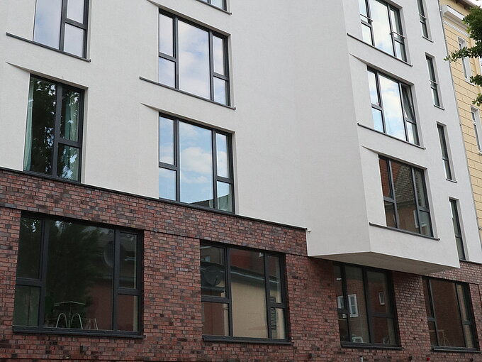 Mehrstöckiges Wohngebäude mit weißen Fassaden und großen Fenstern, Erdgeschoss aus rotem Backstein