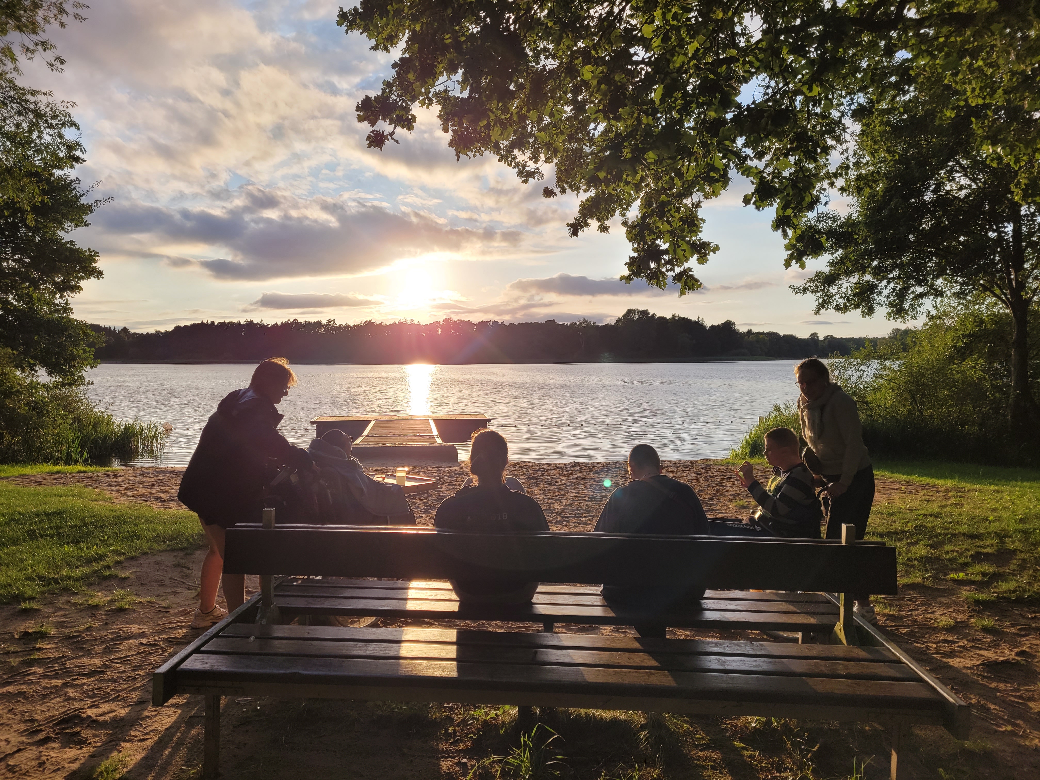 Sonnenuntergang am See. Gruppe von Menschen, ein Mensch im Rollstuhl.