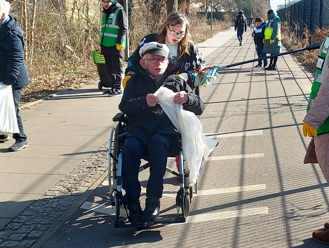 Eine junge Frau und ein Rollstuhlfahrer beim Müllsammeln.