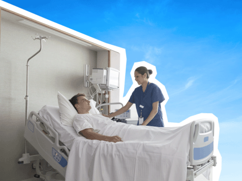 Titelbild: Patient im Krankenhausbett, daneben eine Pflegerin