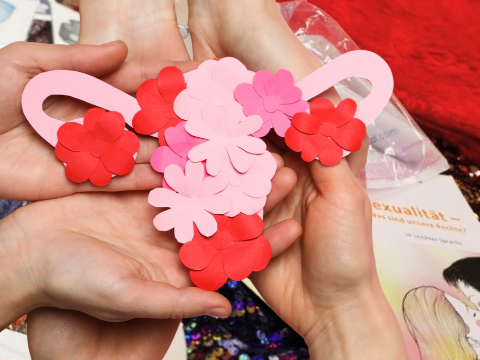 Titelbild zum Workshop Frauengesundheit: mehrere Hände halten einen mit Blüten bestückten Uterus in Papierform